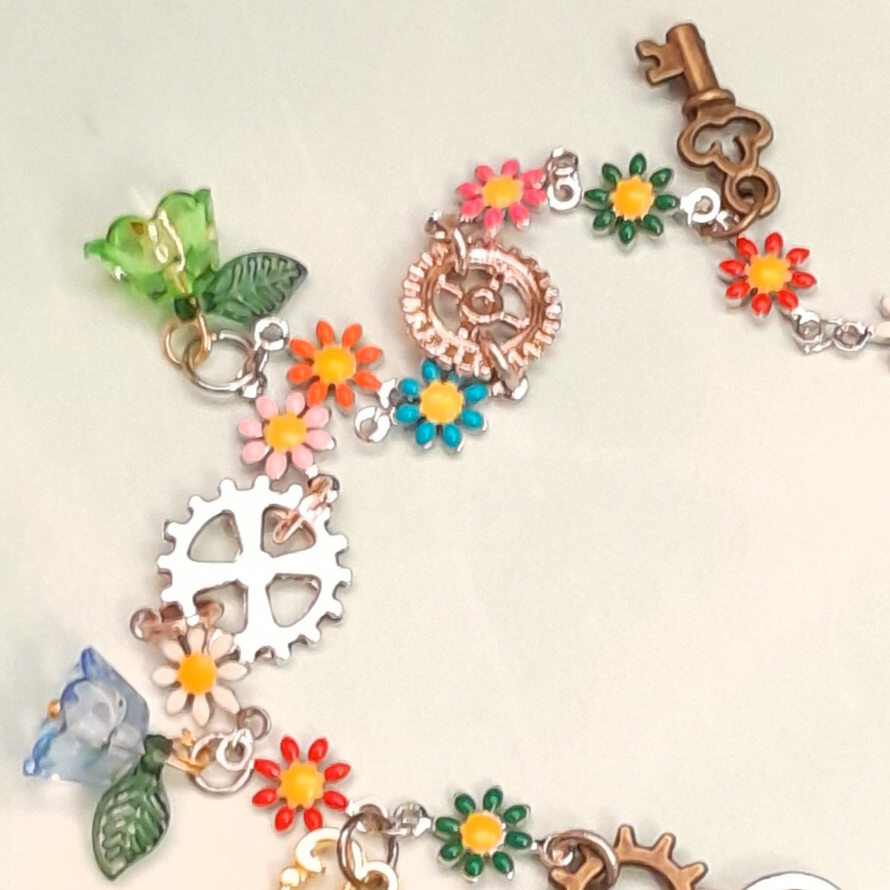Handmade rainbow steampunk charm anklet worn on ankle with vintage keys, gear cog charms, multicolor enamel daisy flowers, and crystal beads, Victorian style vintage style fantasy jewelry
