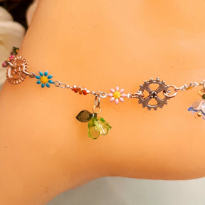 Closeup of handmade steampunk fantasy anklet clasp end showing gear charms, vintage keys, multicolor enamel daisy flowers, blue crystal flower bead, and leaf charms, Victorian style vintage style
