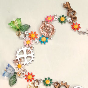 Handmade steampunk fantasy anklet with gear and cog charms, multicolor enamel daisy flowers, green crystal drops, and leaf accents worn on ankle, Victorian style vintage style