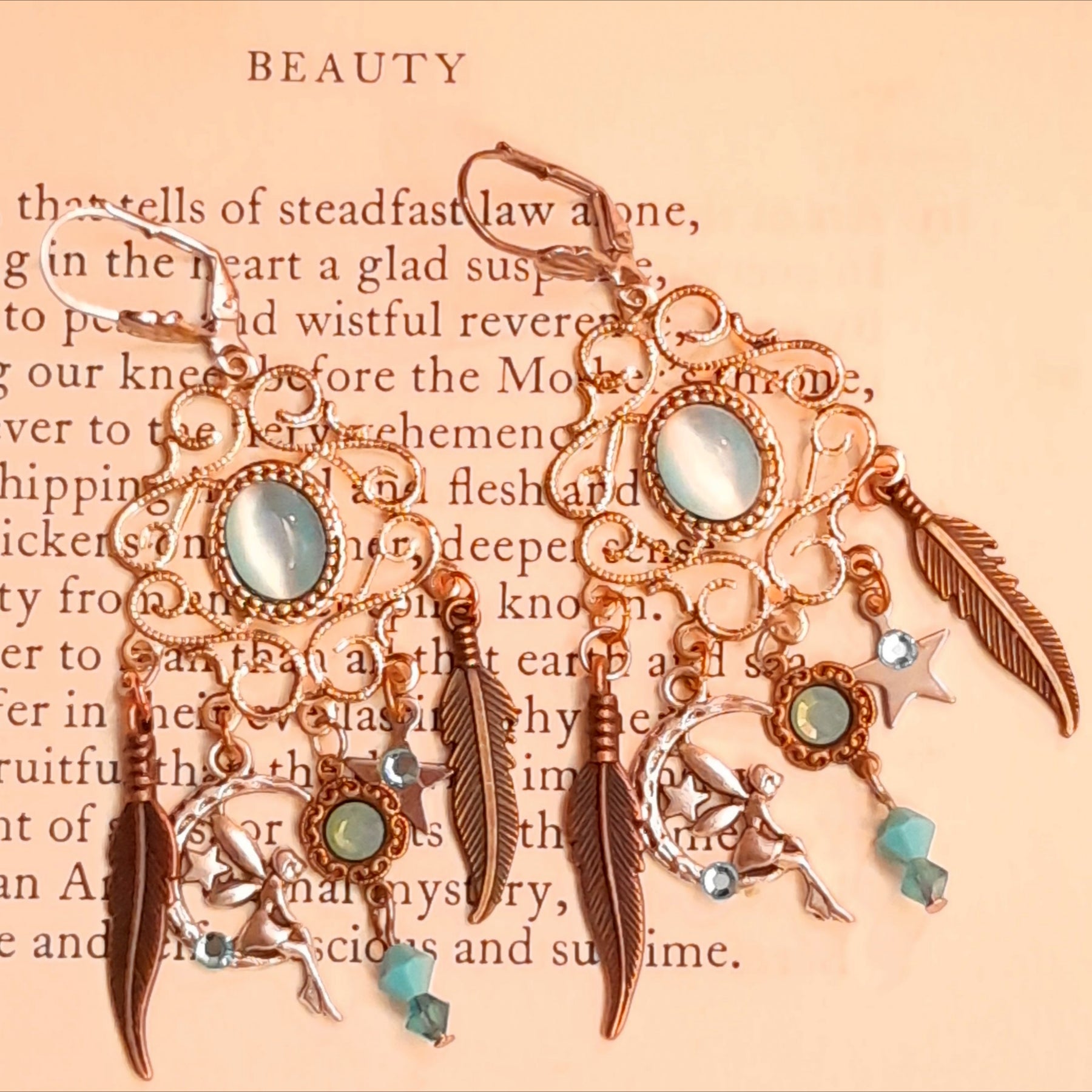 Magical Halloween chandelier earrings featuring glowing oval Cat’s Eye crystals, Pacific Opal and Turquoise Swarovski crystals, fairy-inspired charms, crescent moons, stars, and feather details, Victorian style vintage style jewelry by Rachel Flam Design


