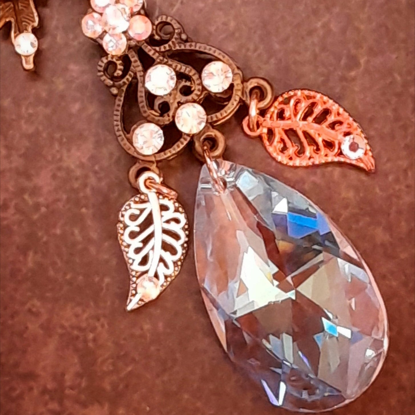 Detail of the Swarovski® crystal teardrop and dangling leaf charms on a Rachel Flam Design Victorian style and vintage style magical necklace, with a sparkling flower and ornate openwork connector.