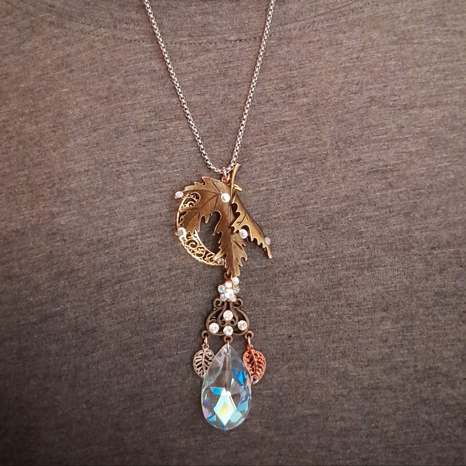 Rachel Flam Design Victorian style and vintage style fantasy statement necklace worn over a gray top, showing the maple leaf, crescent moon, and large Swarovski® crystal teardrop pendant.