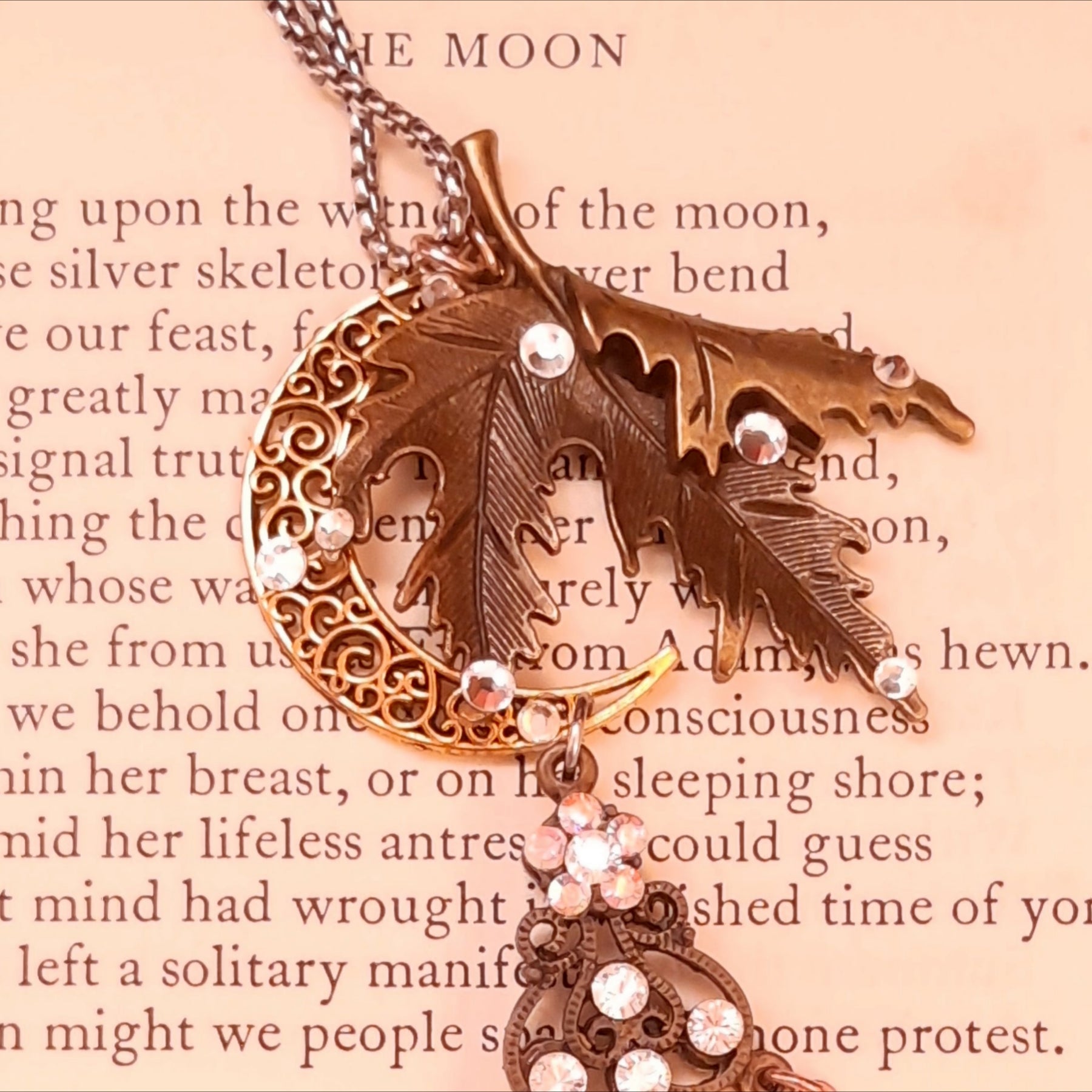 Close-up of the textured maple leaf and openwork crescent moon on a Rachel Flam Design Victorian style and vintage style magical necklace, embellished with Crystals by Swarovski® on a poetry page.
