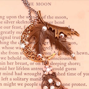 Close-up of the textured maple leaf and openwork crescent moon on a Rachel Flam Design Victorian style and vintage style magical necklace, embellished with Crystals by Swarovski® on a poetry page.