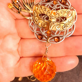 Masquerade necklace decorated with an intricate mask, ornate filigree, fiery orange Swarovski crystals, and a faceted Citrine crystal ball, nature-inspired Halloween jewelry in Victorian style and vintage style by Rachel Flam Design