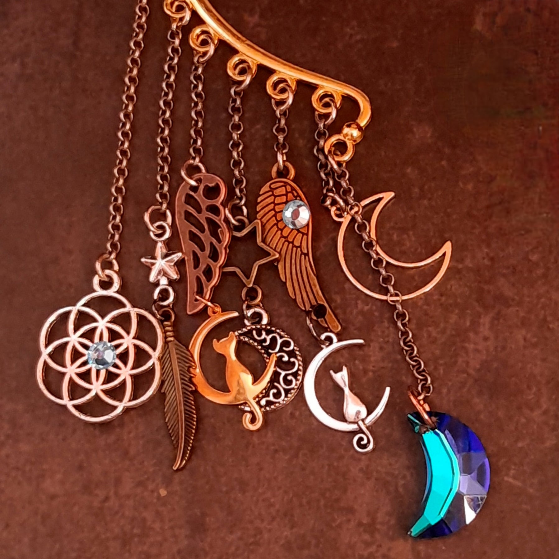Close up of a Victorian style and vintage style ear wrap by Rachel Flam Design, featuring cats inside crescents, wing and feather charms, Swarovski crystals and a faceted blue moon drop.