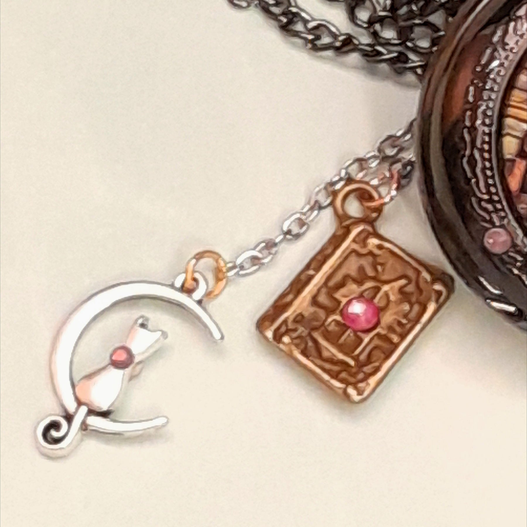 Close up of cat on moon charm and copper book charm with Swarovski pink crystal accents on handmade fantasy necklace Victorian style vintage style