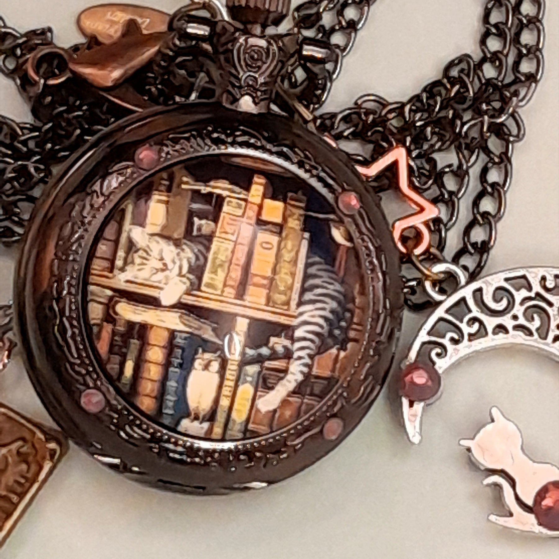 Detail of handmade magical fantasy pocket watch necklace showing cat and books scene with Swarovski purple crystals and antiqued brass chain Victorian style vintage style