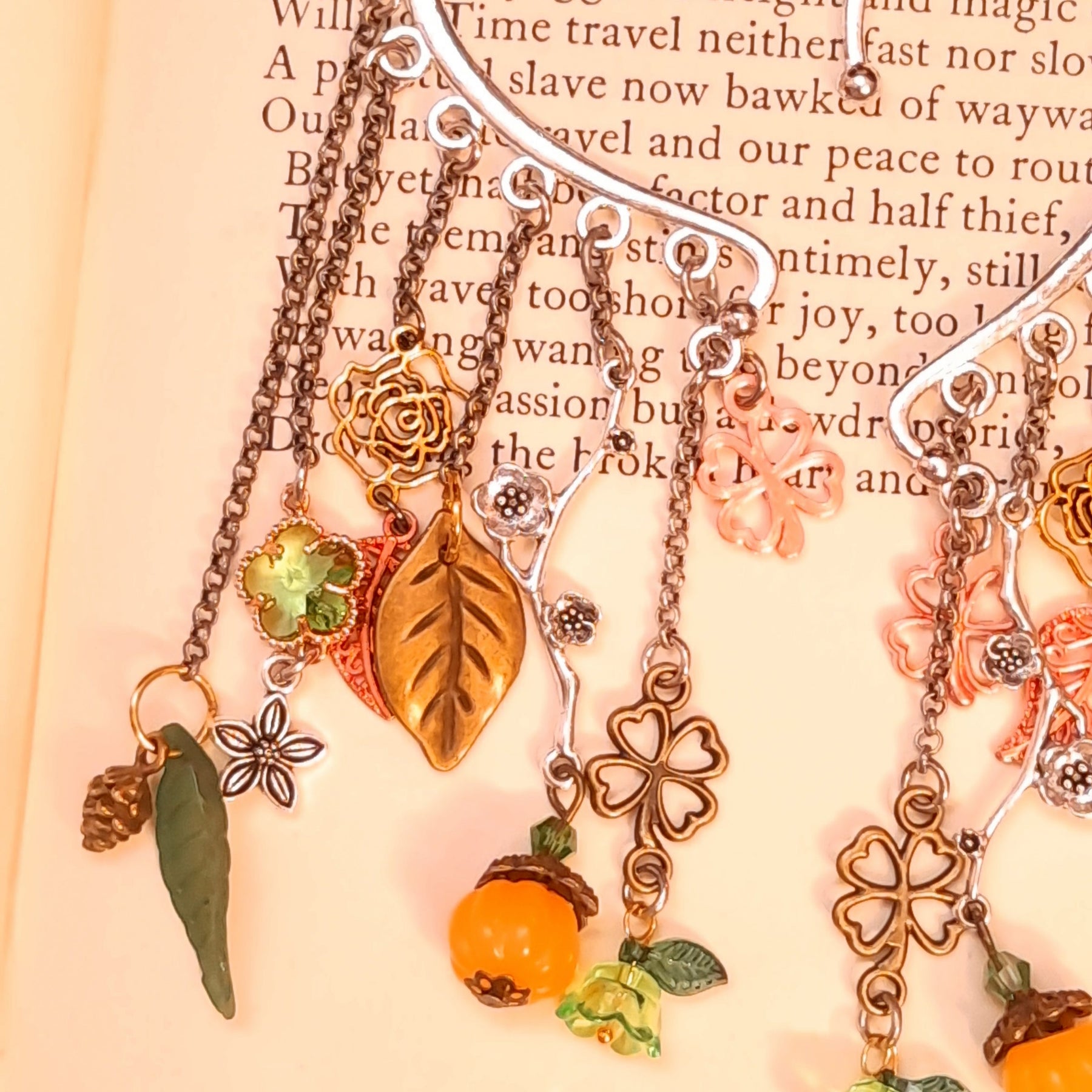 Close up of Victorian style and vintage style non pierced ear wraps by Rachel Flam Design, with green Swarovski crystals, rose charms, floral branches and pumpkin drops on a book.