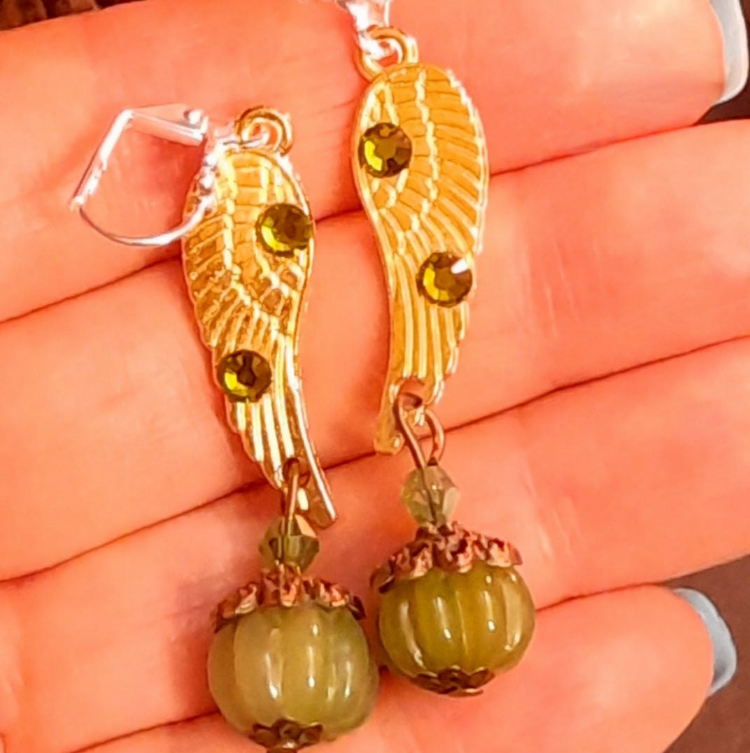 Victorian style vintage style angel wing earrings with sparkling Swarovski Olivine crystals and ribbed pumpkin drops shown against a hand, handmade fantasy jewelry by Rachel Flam Design