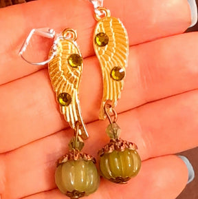 Victorian style vintage style angel wing earrings with sparkling Swarovski Olivine crystals and ribbed pumpkin drops shown against a hand, handmade fantasy jewelry by Rachel Flam Design