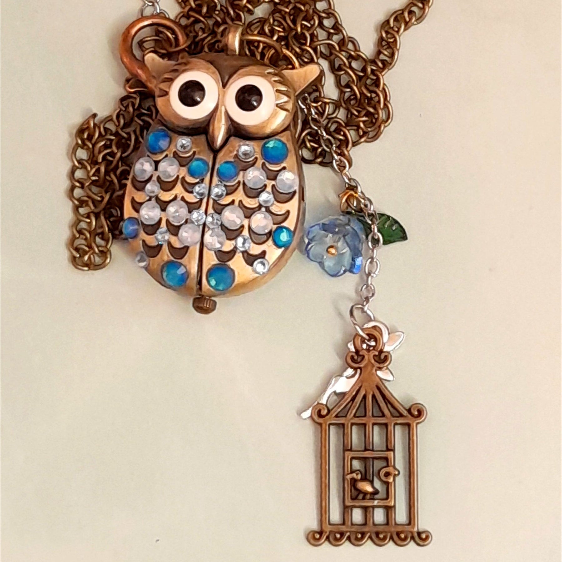 Cute owl pocket watch necklace flat lay full view with chain blue flower fairy bird cage charm Swarovski blue crystals animal jewelry Victorian style vintage style handmade Rachel Flam Design