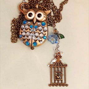 Cute owl pocket watch necklace flat lay full view with chain blue flower fairy bird cage charm Swarovski blue crystals animal jewelry Victorian style vintage style handmade Rachel Flam Design