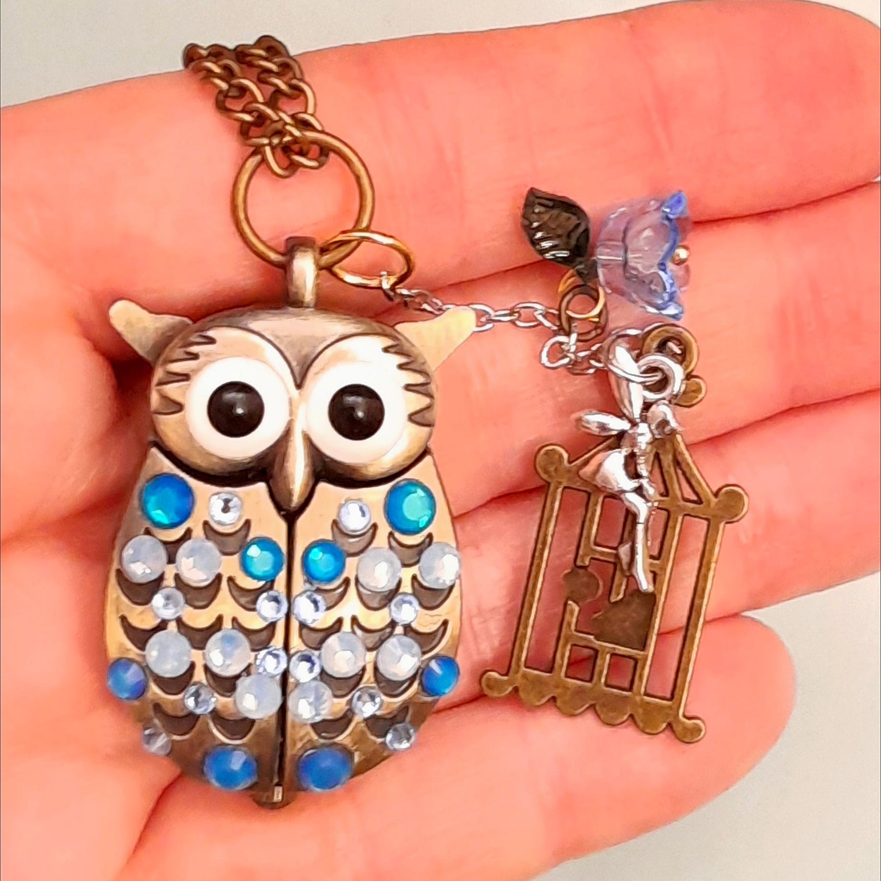 Cute owl pocket watch necklace held in hand showing blue flower fairy bird cage charms Swarovski blue crystals animal jewelry Victorian style vintage style handmade Rachel Flam Design