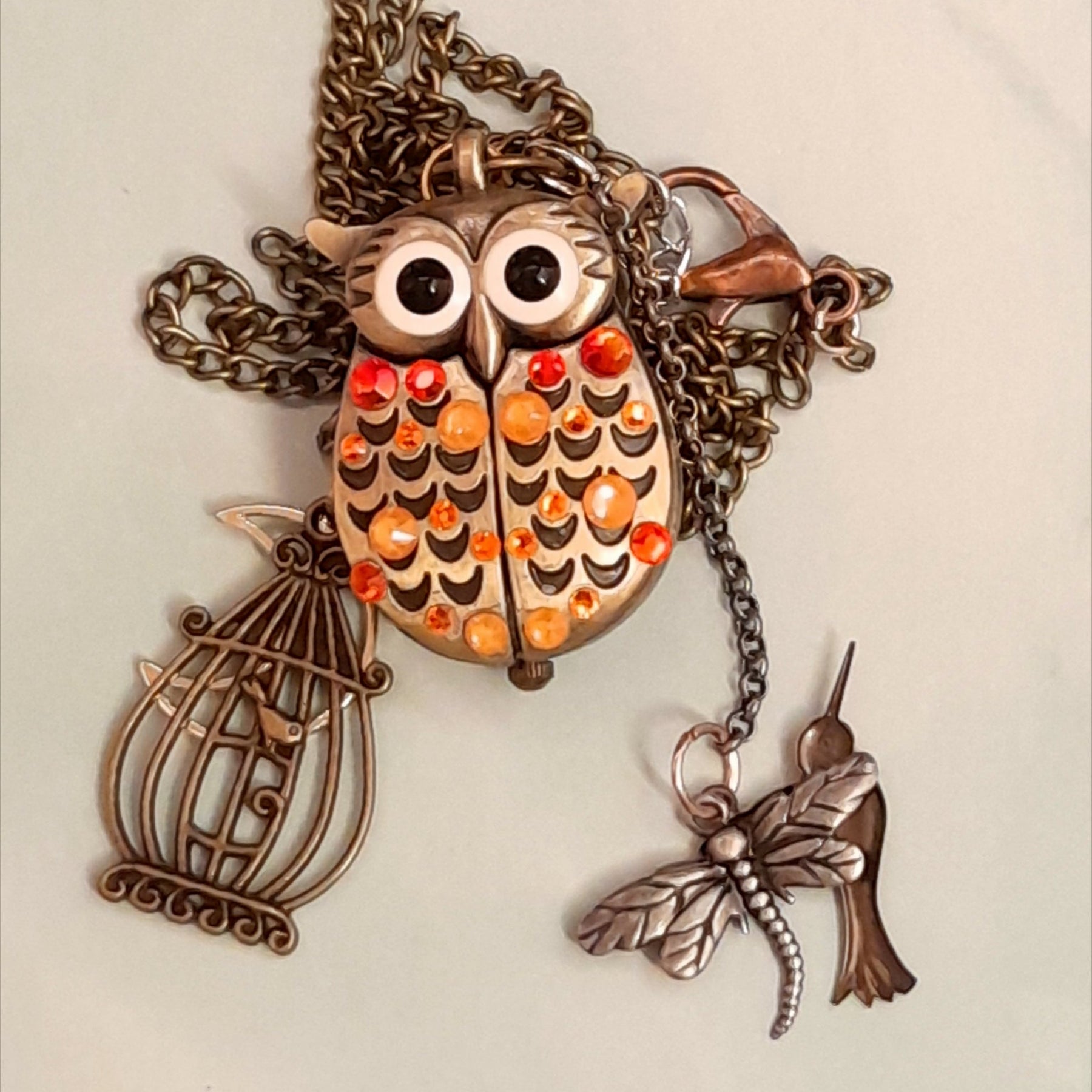 Cute owl pocket watch necklace flat lay full view with birdcage dragonfly hummingbird charms Swarovski orange crystals animal jewelry Victorian style vintage style handmade Rachel Flam Design
