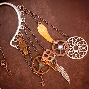 Detailed view of a Rachel Flam Design steampunk ear wrap and ear cuff embellished with light blue Swarovski® crystals, featuring a wing, feather, gears, keys, and an openwork circle in Victorian style and vintage style.