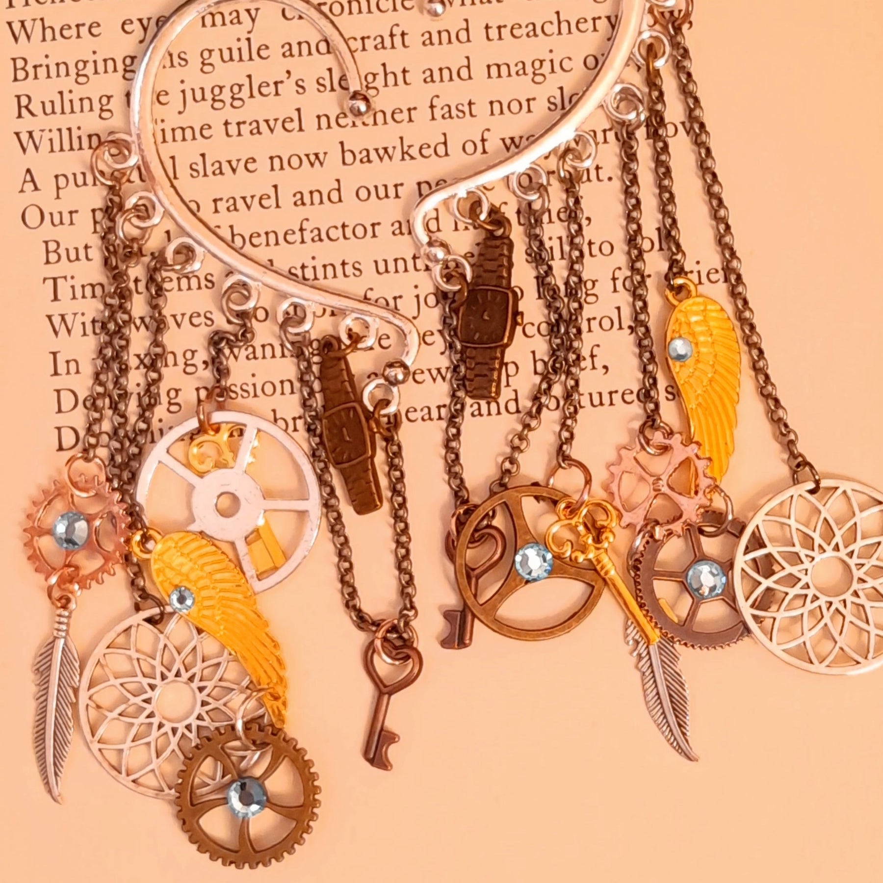 Rachel Flam Design steampunk ear wraps and ear cuffs displayed beneath pinecones, with light blue Swarovski® crystals and cascading clockwork, key, wing, and feather charms in Victorian style and vintage style.