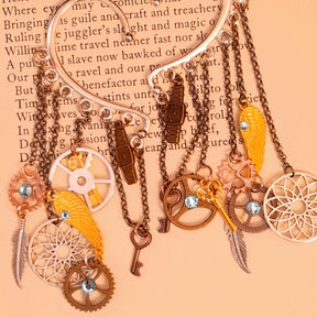Rachel Flam Design steampunk ear wraps and ear cuffs displayed beneath pinecones, with light blue Swarovski® crystals and cascading clockwork, key, wing, and feather charms in Victorian style and vintage style.
