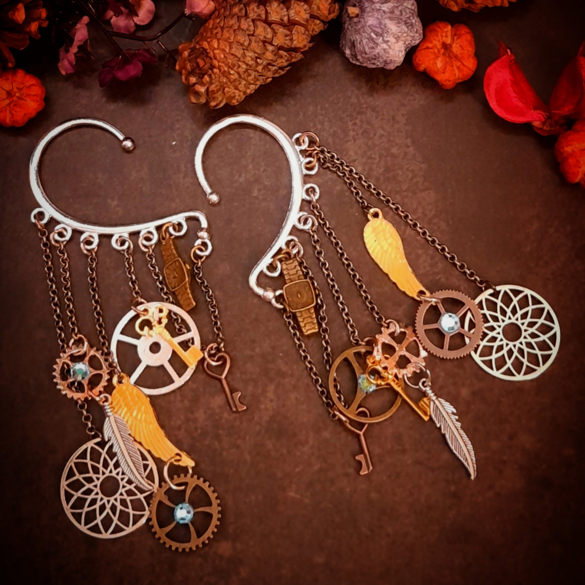 Rachel Flam Design steampunk ear wraps and ear cuffs with light blue Swarovski® crystals, gears, keys, wings, and feathers, combining Victorian style and vintage style on a dark background.