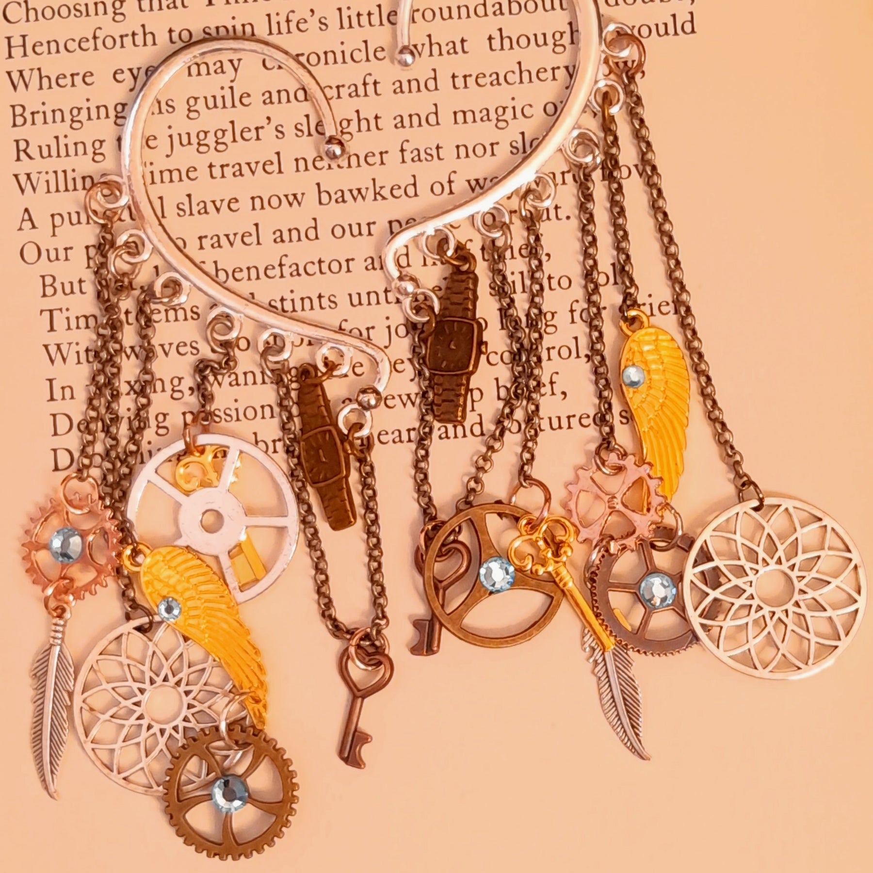 Steampunk ear wraps and ear cuffs by Rachel Flam Design, created with light blue Swarovski® crystals and dangling watch, gear, key, wing, and feather charms, in Victorian style and vintage style on a book page.