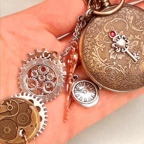 Steampunk pocket watch necklace held in hand showing all charms including steampunk gears watch movement disc skeleton key and mini quartz watch charm antiqued brass Victorian style vintage style fantasy handmade

