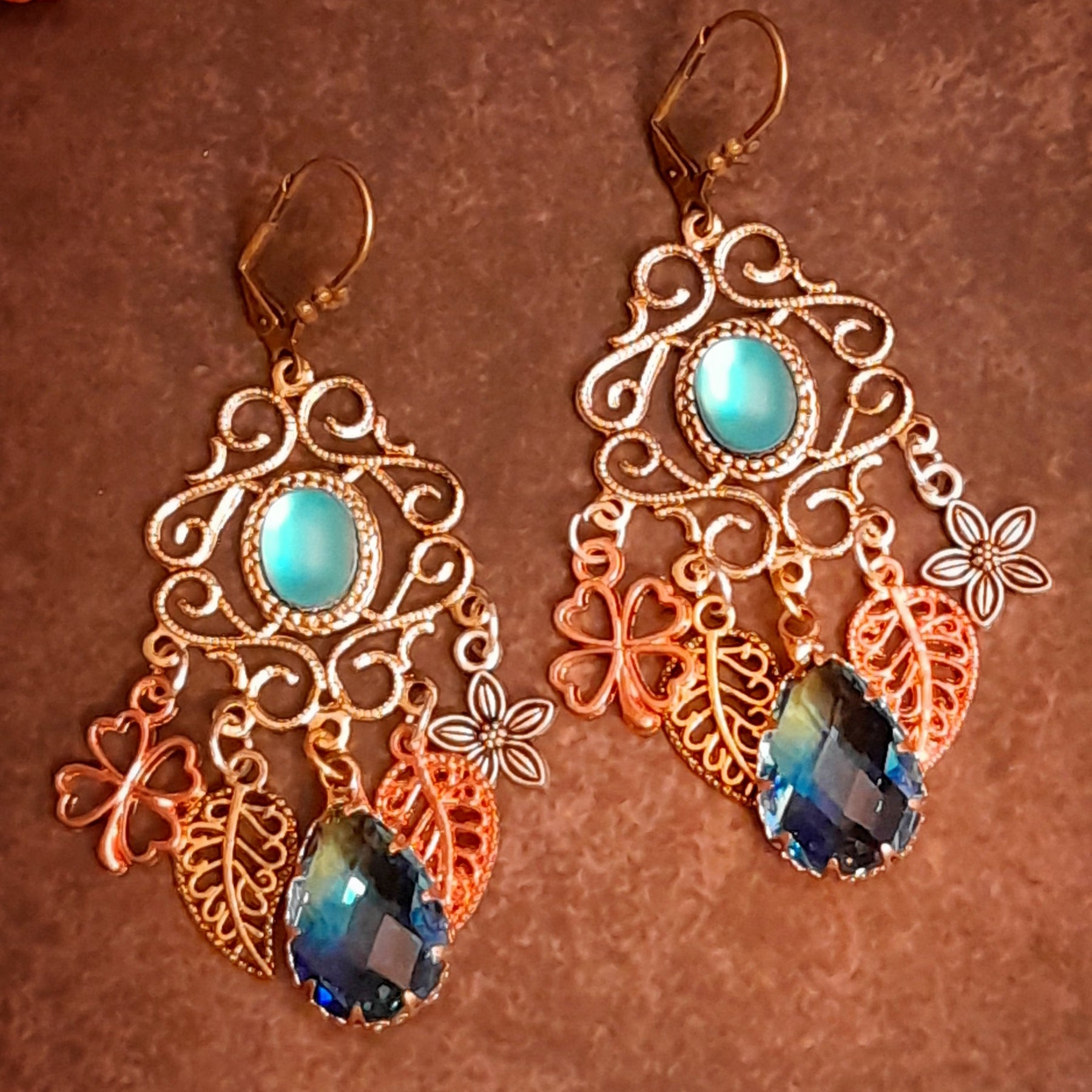 Victorian style and vintage style botanical chandelier earrings with glowing turquoise cat eye cabochons, layered flowers, leaves, and colorful glass drops by Rachel Flam Design
