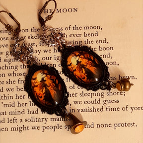 Witchy dangle earrings with a tiny witch riding a broom through a crescent moon, glowing orange Swarovski crystals, witch hat and cauldron dangles, Victorian style and vintage style fantasy jewelry by Rachel Flam Design