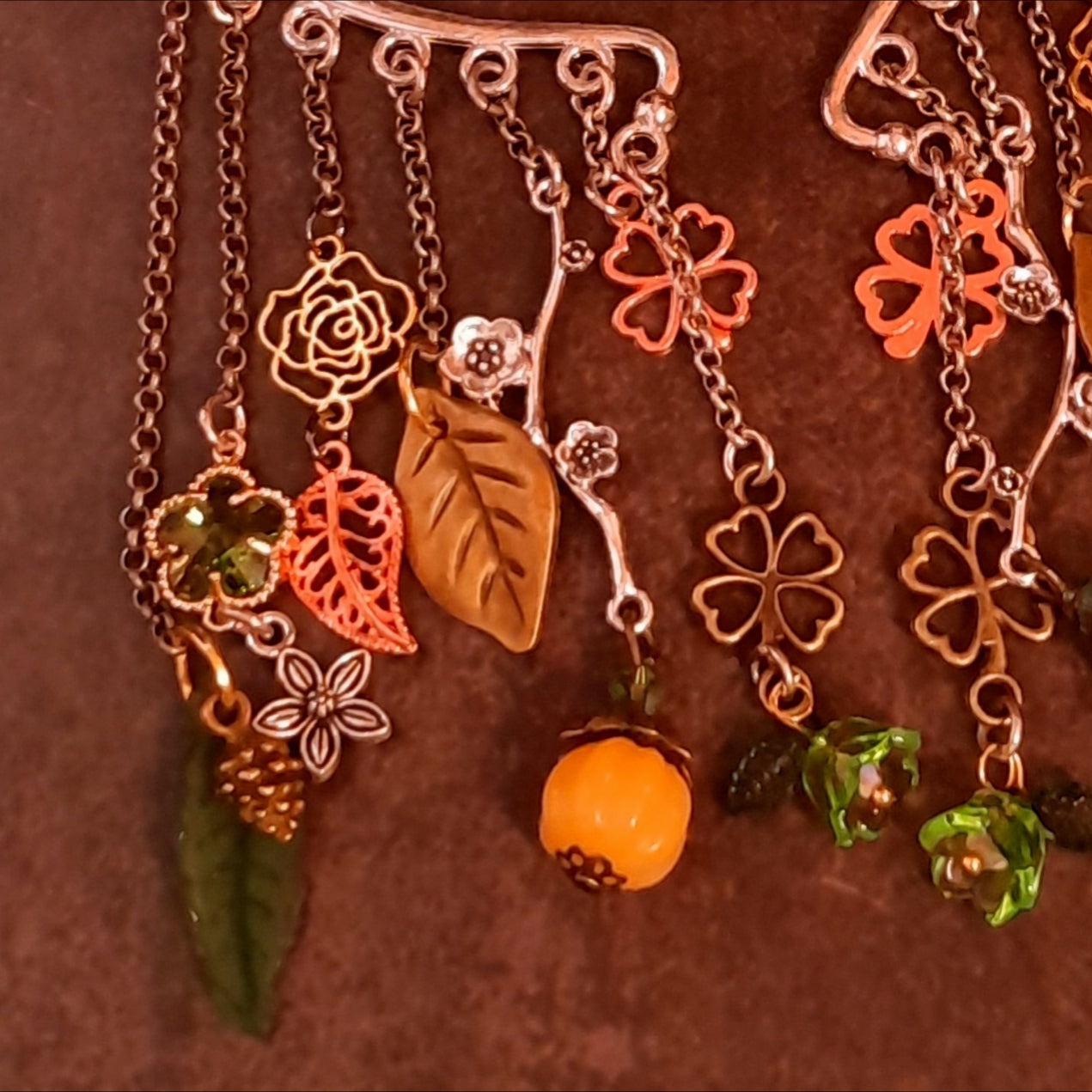 Close up of Victorian style and vintage style ear wrap cuffs by Rachel Flam Design, showing green Swarovski crystals, openwork roses, leaves, pinecone charms and orange pumpkin drops.