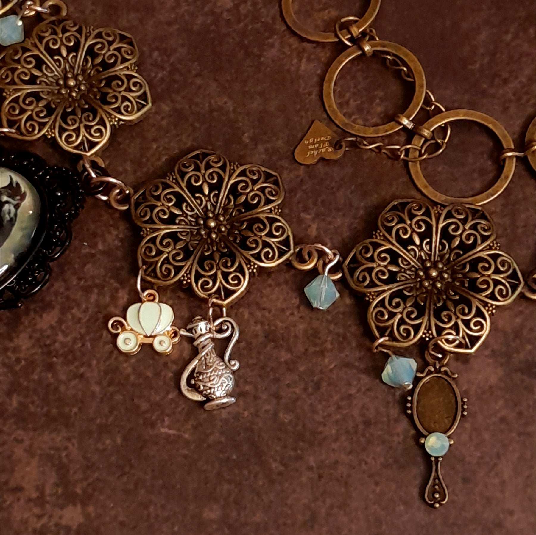 Detail of layered charm cluster surrounding the black crow cabochon, Pumpkin carriage magical genie lamp magical hand mirror, Victorian style vintage style Swarovski crystal necklace, Rachel Flam Design