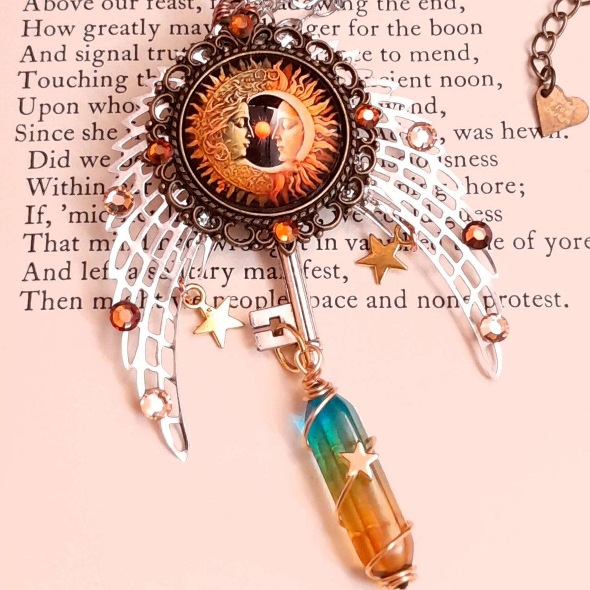sun and moon cabochon nestled between silver wings. adorned with brown and gold swarovski crystals and golden stars. a color changing crystal wrapped with star at the bottom