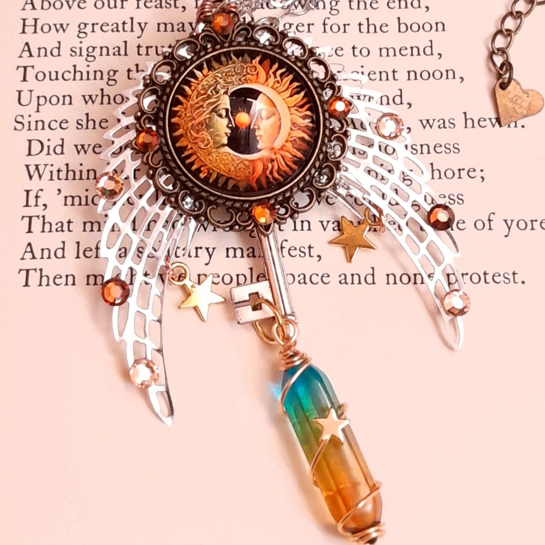 sun and moon cabochon nestled between silver wings. adorned with brown and gold swarovski crystals and golden stars. a color changing crystal wrapped with star at the bottom