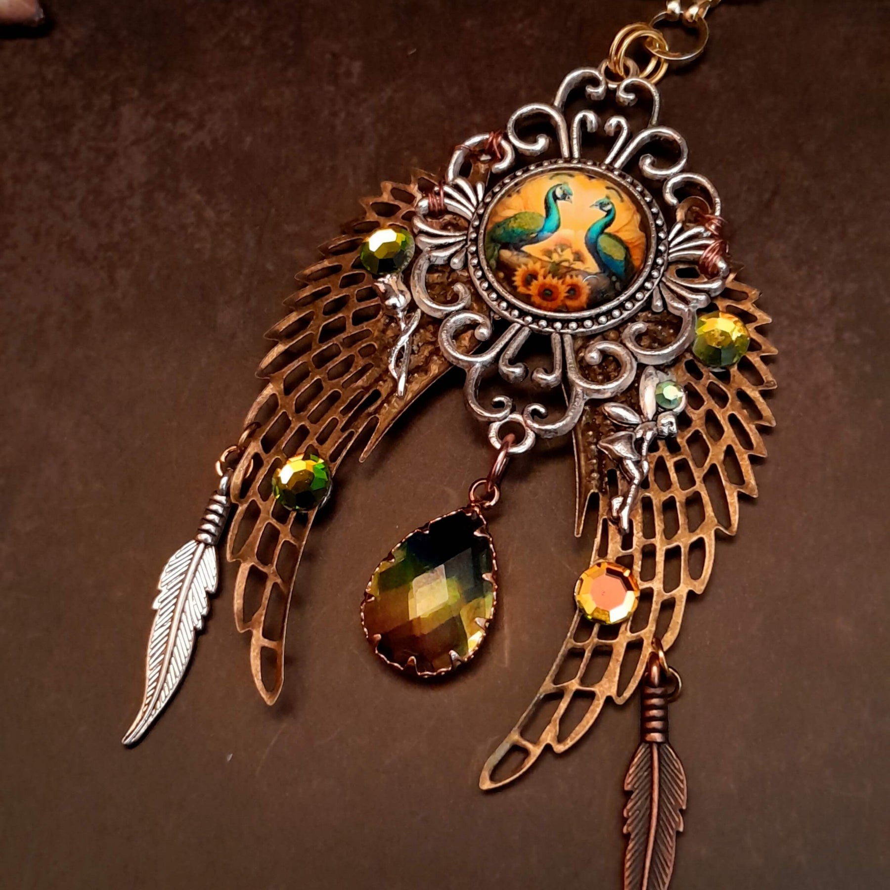 victorian style necklace with a peacock cabochon. Bright golden yellow and green crystals. Feather accents, a fairy, and a striking teardrop crystal