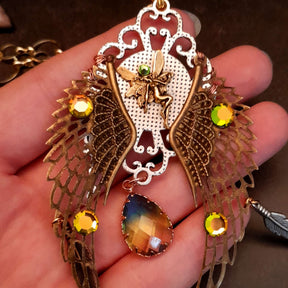 victorian style necklace with a peacock cabochon. Bright golden yellow and green crystals. Feather accents, a fairy, and a striking teardrop crystal